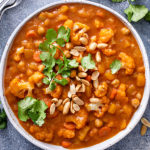 Bowl of cauliflower curry with herbs and cashew nuts on top